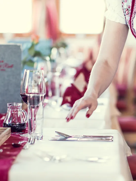 Kellnerin im traditionellen Dirndl deckt einen Tisch in einem bayerischen Restaurant