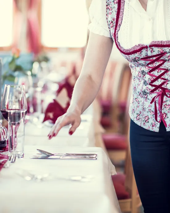 Waitress in traditional dirndl setting a table in a Bavarian-style restaurant