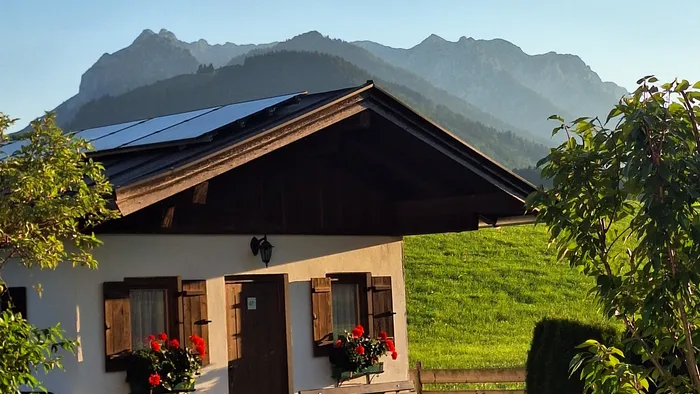 Kleines Häuschen mit roten Blumen, Solarpaneelen und Bergblick im Sonnenuntergang