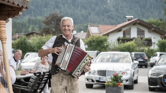 Mann in bayerischer Tracht spielt Akkordeon im Freien nahe einem Alpendorf