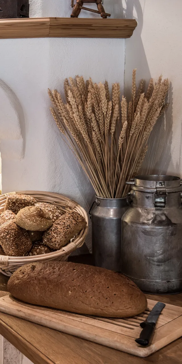 Rustic kitchen corner with assorted fresh bread, grain stalks, and vintage milk jugs