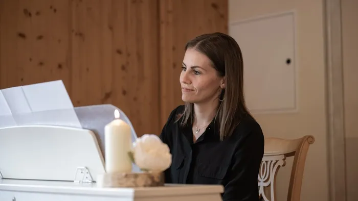 Woman in black blouse sitting at white piano with candle and flower decoration