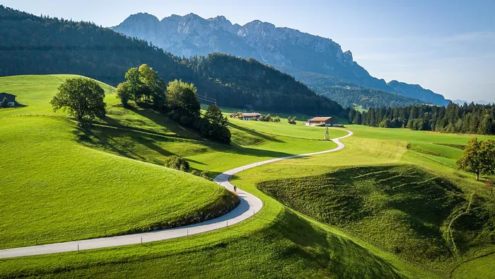 Curving country road through green meadows with alpine mountains in the background