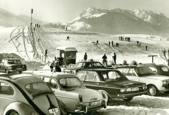 Skigebiet im Retro-Stil mit Skifahrern am Hang und Oldtimern im Vordergrund