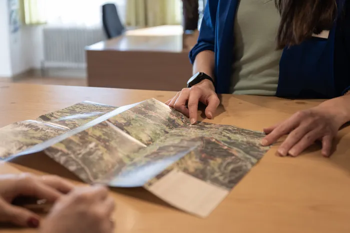 Two people examining a hiking trail map at a wooden desk in a tourist office
