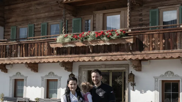 Familie in traditioneller bayerischer Kleidung vor rustikalem Alpen-Gasthaus mit Blumenbalkonen