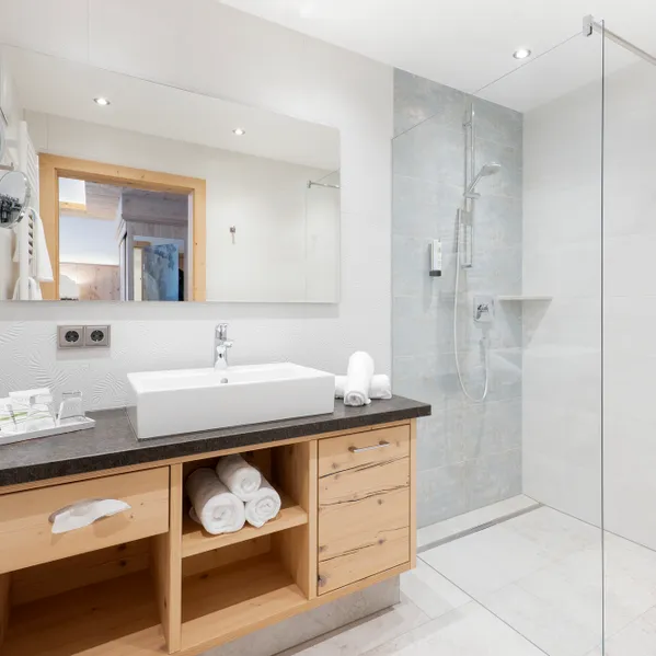 Modernes Hotelbad mit begehbarer Dusche, Waschtisch aus Holz, großem Spiegel und weißen Fliesen