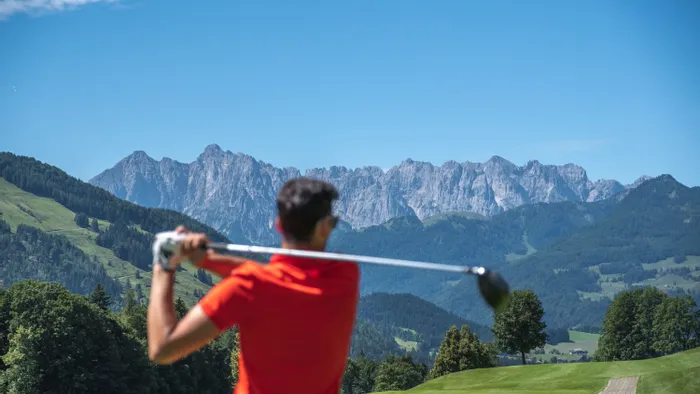 Golfer in red shirt swinging club on mountain golf course under clear blue sky