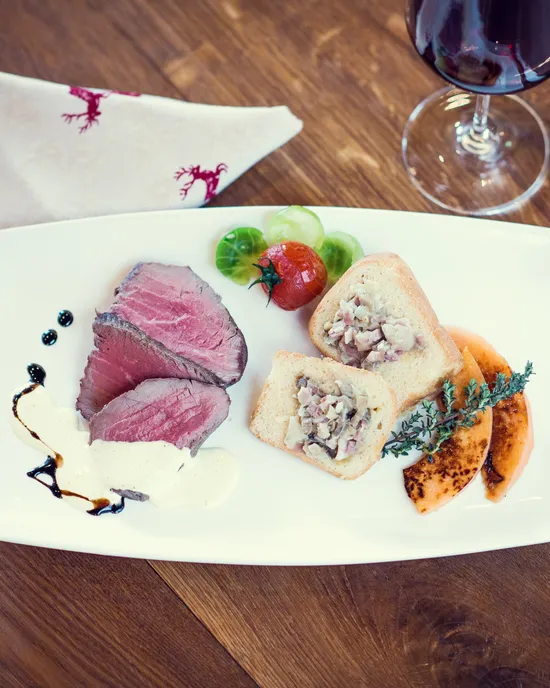 Gourmet beef slices with creamy sauce, vegetable-stuffed bread, grapes, and red wine on wooden table