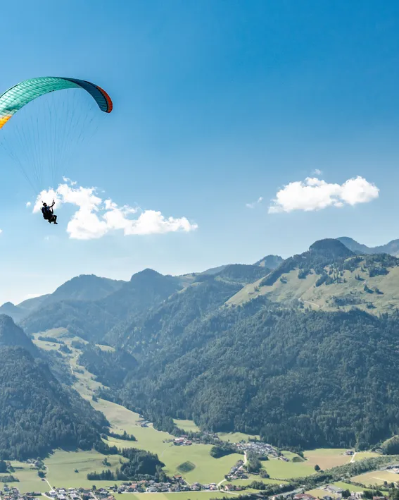 Paraglider soaring above alpine mountains on a clear sunny day near a small village