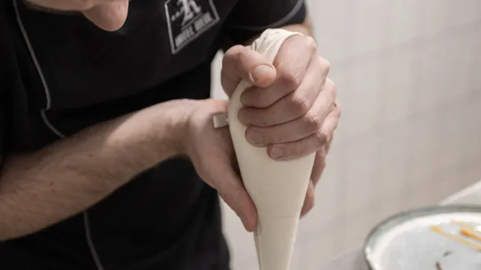 Pastry chef decorating gourmet dessert with cream on a ceramic plate in professional kitchen