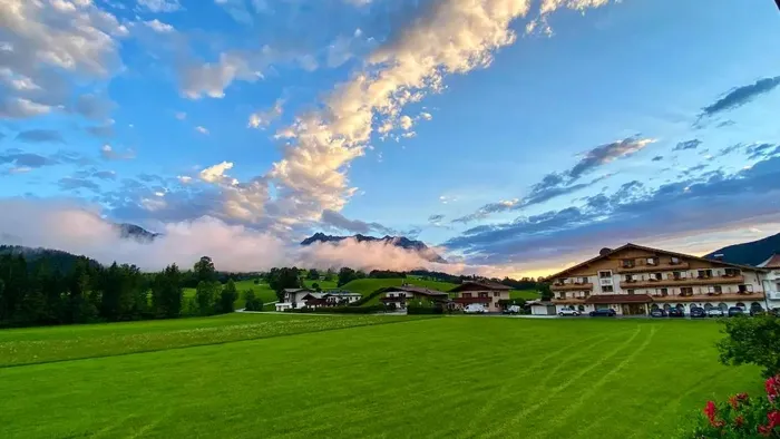 Alpenhotel mit grüner Wiese und Bergblick unter dramatischem Abendhimmel