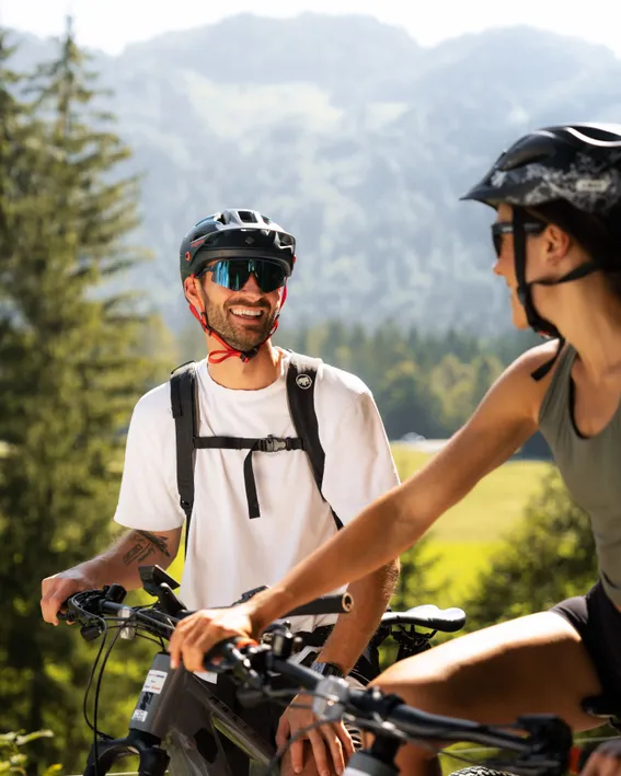 Smiling couple riding mountain bikes with helmets in sunny alpine landscape