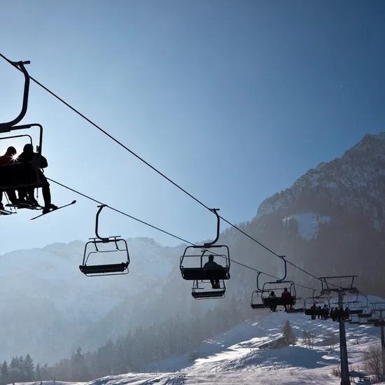 Skiers riding a chairlift over a snowy mountain slope under clear blue sky