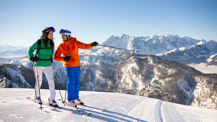 Couple in colorful ski gear enjoying sunny day on snow-covered alpine slope