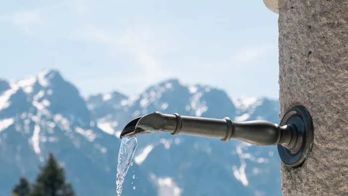 Water flowing from a rustic fountain spout with snow-capped mountains in the background