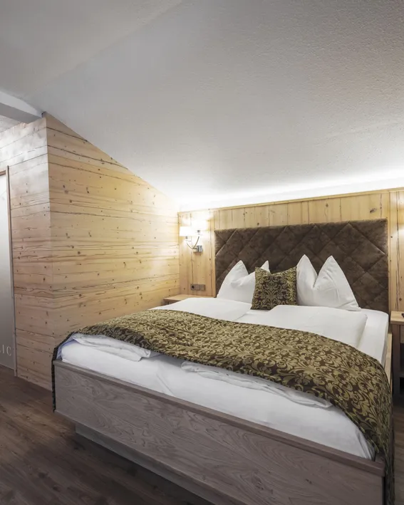 Gemütliches Hotelzimmer mit Holzverkleidung, Doppelbett und Zierkissen im Alpenstil