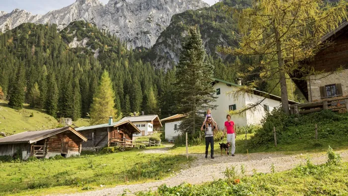 Family hiking near alpine cabins in the Austrian mountains with forest and rocky peaks