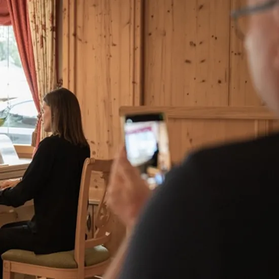 Frau spielt E-Piano in gemütlichem Holzraum, während ein Mann mit dem Smartphone filmt