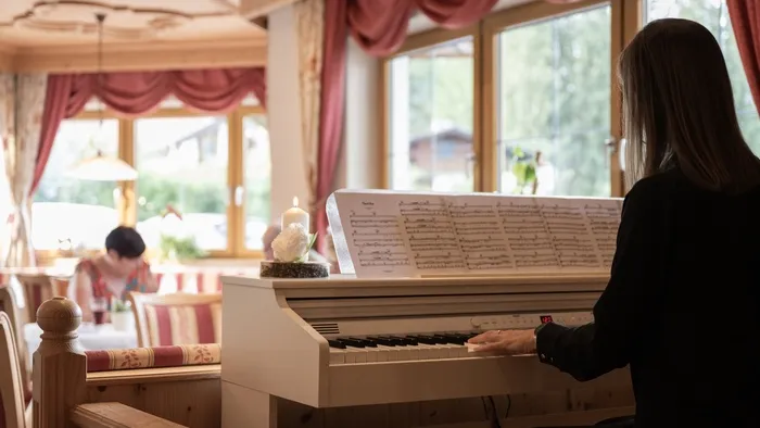 Frau spielt Klavier in gemütlichem Restaurant mit Notenblatt und großen Fenstern
