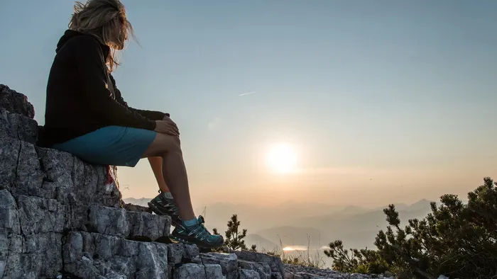 Frau sitzt auf Felsen in den Bergen und blickt ins Tal bei Sonnenuntergang