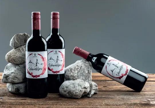 Three bottles of Schwindelfrei red wine with mountain label on rustic wood and stones