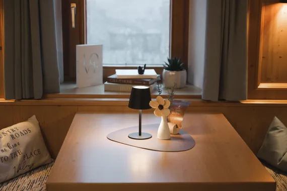 Gemütlicher Raum mit Holztisch, Lampe, Vase mit Blume, Büchern und Deko am Fenster