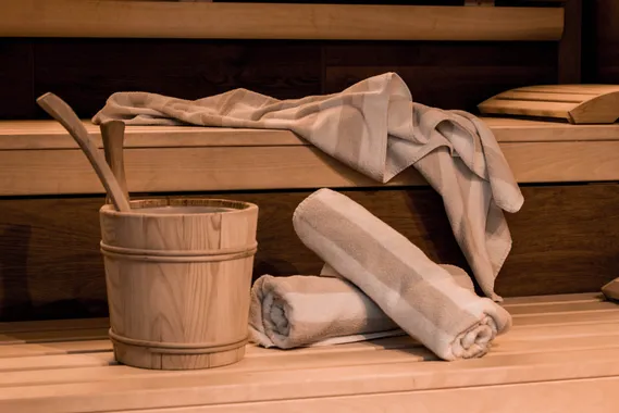 Sauna-Innenraum mit gerollten Handtüchern, Holzeimer und Kelle auf hellen Holzbänken