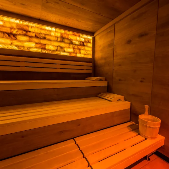 Moderne Holzsauna mit warmer Beleuchtung und einem Eimer auf der Bank