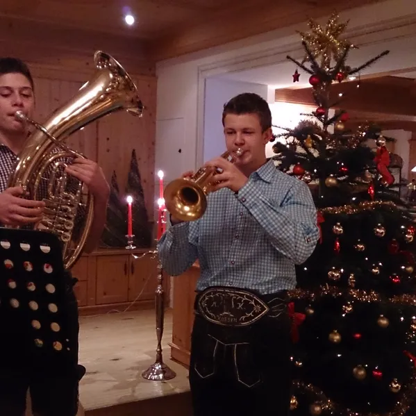 Zwei junge Musiker spielen Blechblasinstrumente neben geschmücktem Weihnachtsbaum im Innenraum