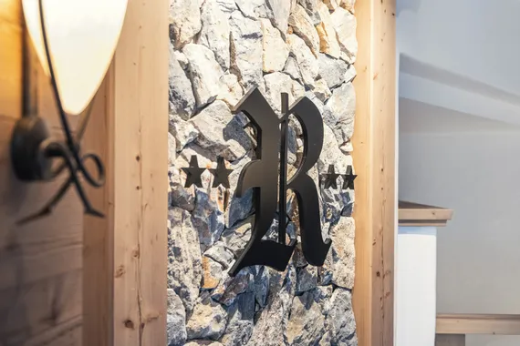Dekorativer schwarzer Buchstabe R mit Sternen an Steinwand in rustikalem Holzinterieur