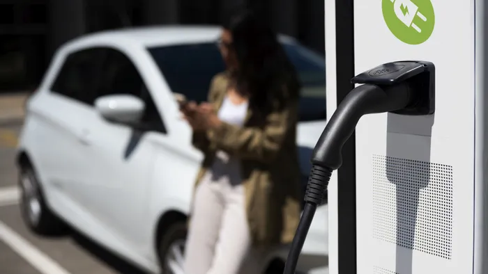 Electric car charging at station with woman using smartphone nearby