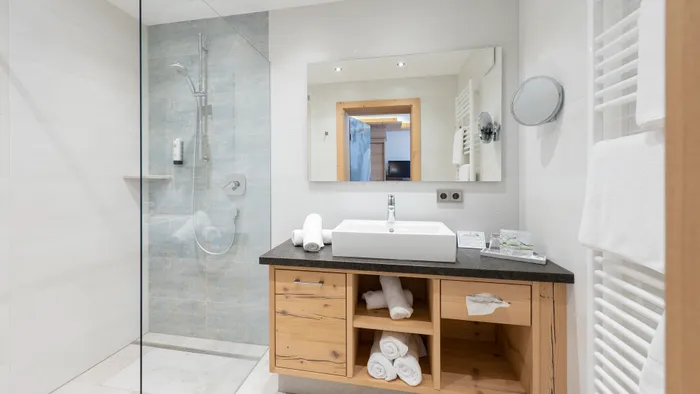 Modernes Hotelbad mit begehbarer Dusche, Holzwaschtisch und gerollten weißen Handtüchern
