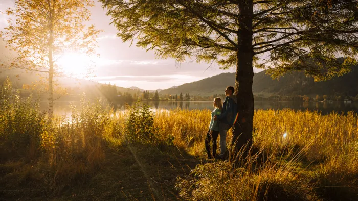 Paar steht unter Baum am Bergsee bei Sonnenuntergang im Herbst