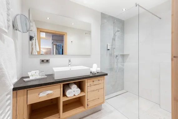 Modernes Hotelbad mit begehbarer Dusche, Waschtisch aus Holz, großem Spiegel und weißen Fliesen