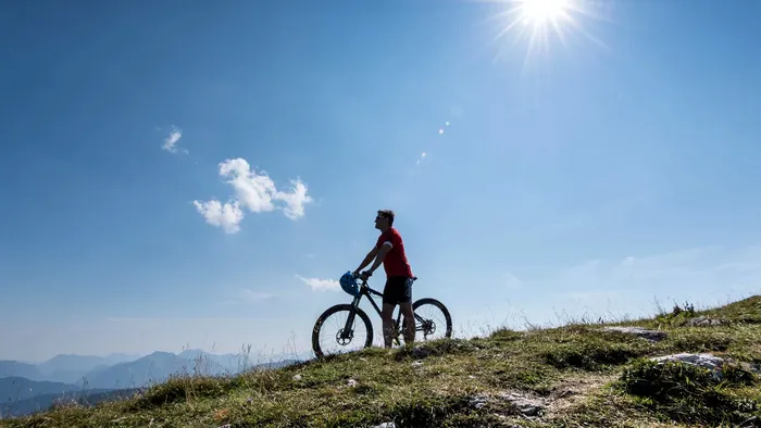 Man with mountain bike standing on grassy hill under bright sun