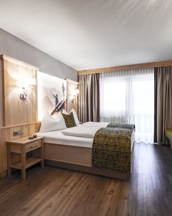 Modernes Alpenhotelzimmer mit Doppelbett, Holzmöbeln und Bergmotiv-Dekor