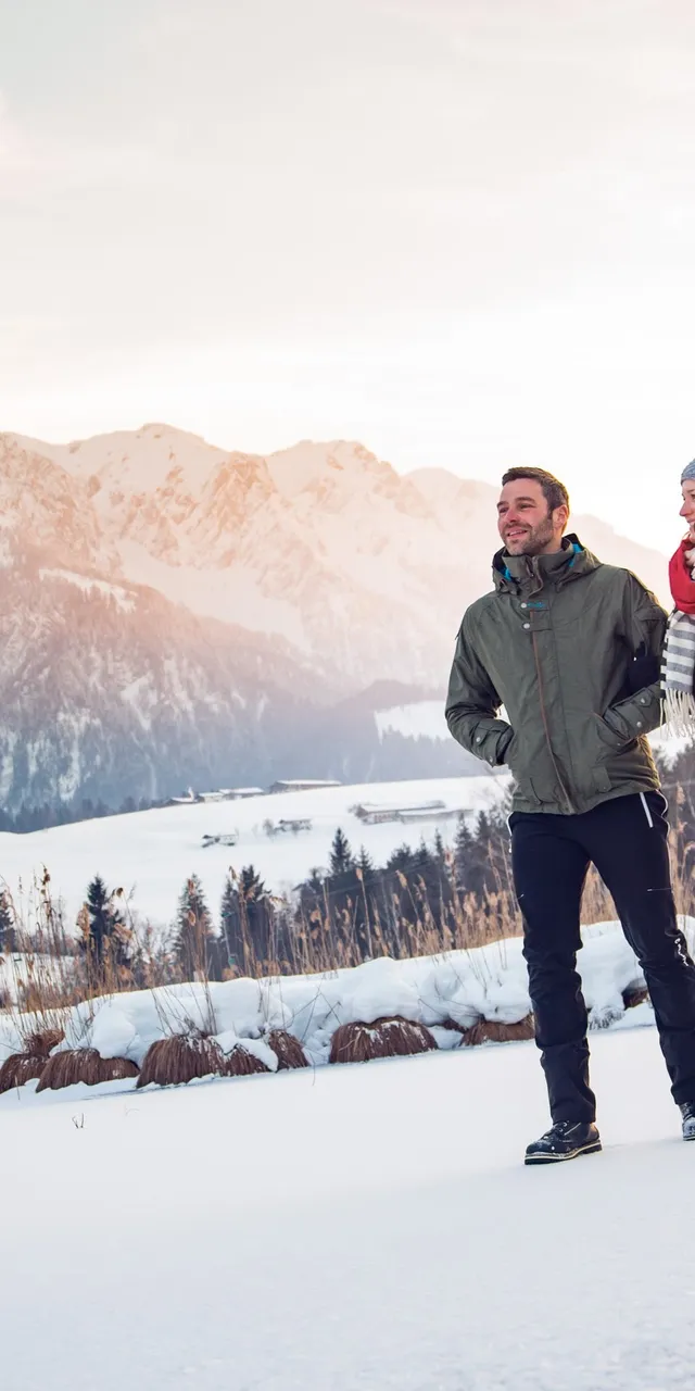 Gruppe von Menschen beim Winterwandern durch verschneite Alpenlandschaft bei Sonnenuntergang