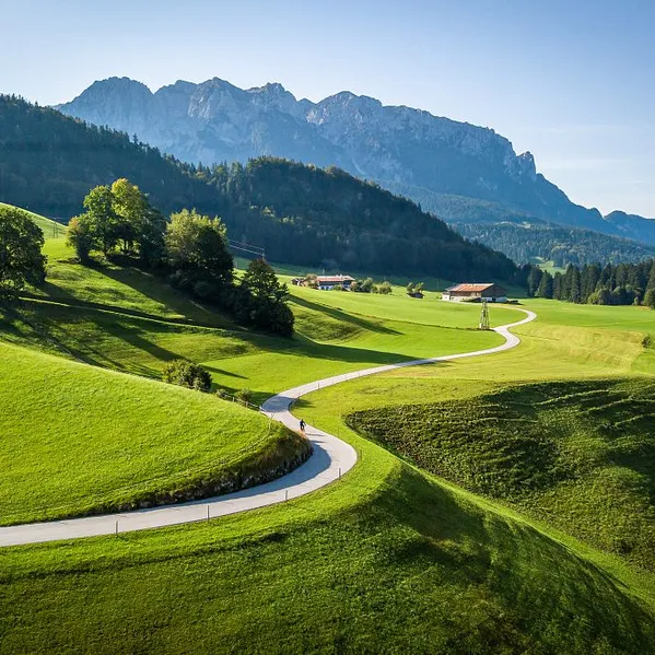 Curving country road through green meadows with alpine mountains in the background