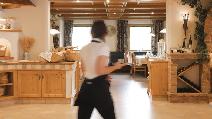 Kellner geht durch ein gemütliches Restaurant mit Holzdekor und warmer Beleuchtung