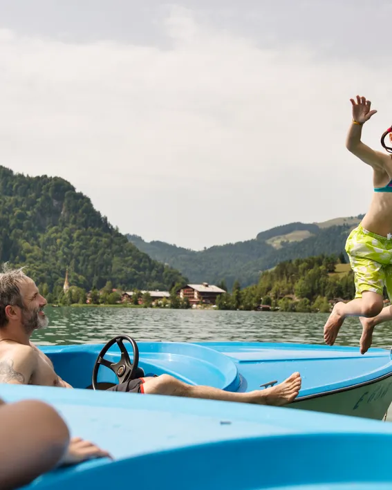 Child jumping from paddle boat into mountain lake on summer day
